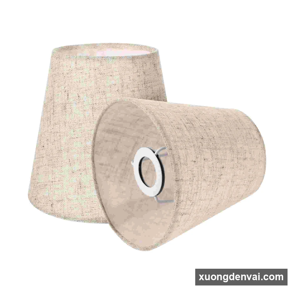Cặp hai chụp đèn vải linen mộc dáng nón cụt đặt cạnh nhau, một chiếc nằm nghiêng lộ vòng gắn đui bên trong