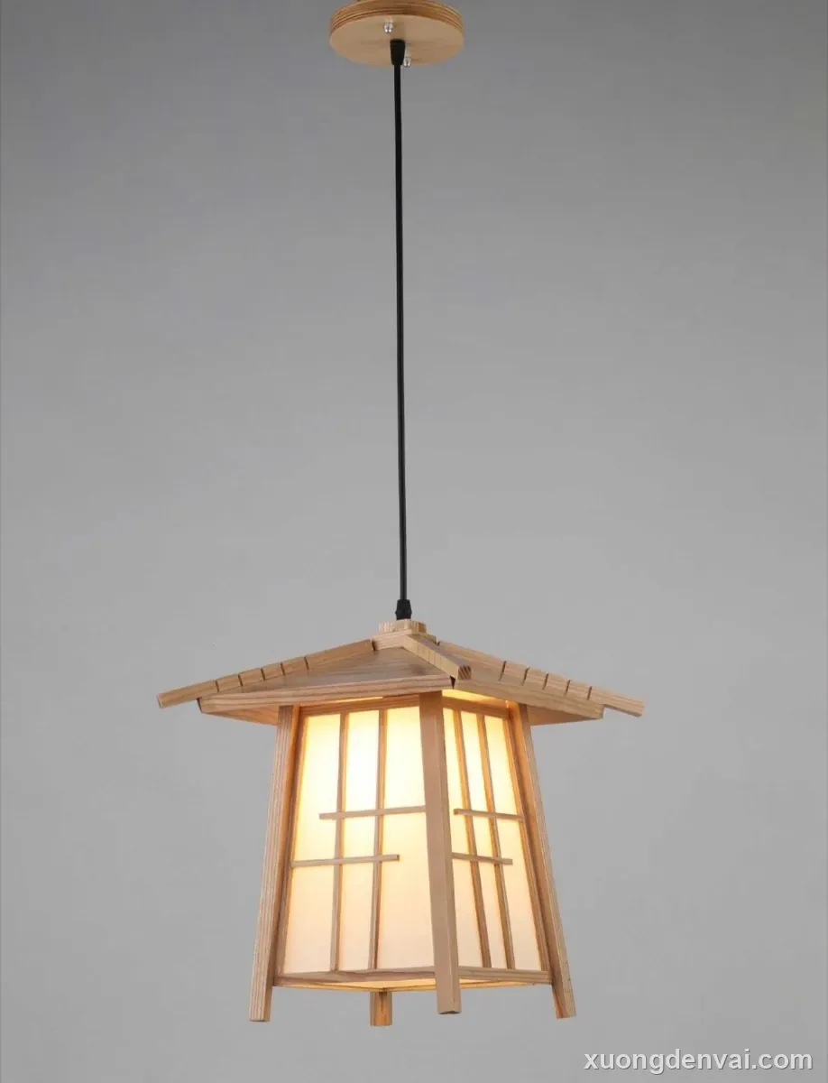 Đèn lồng gỗ dáng mái nhà kiểu Nhật màu gỗ sáng, treo thả trần bằng dây điện đen, ánh sáng vàng ấm hắt qua mặt kính mờ có thanh chắn caro