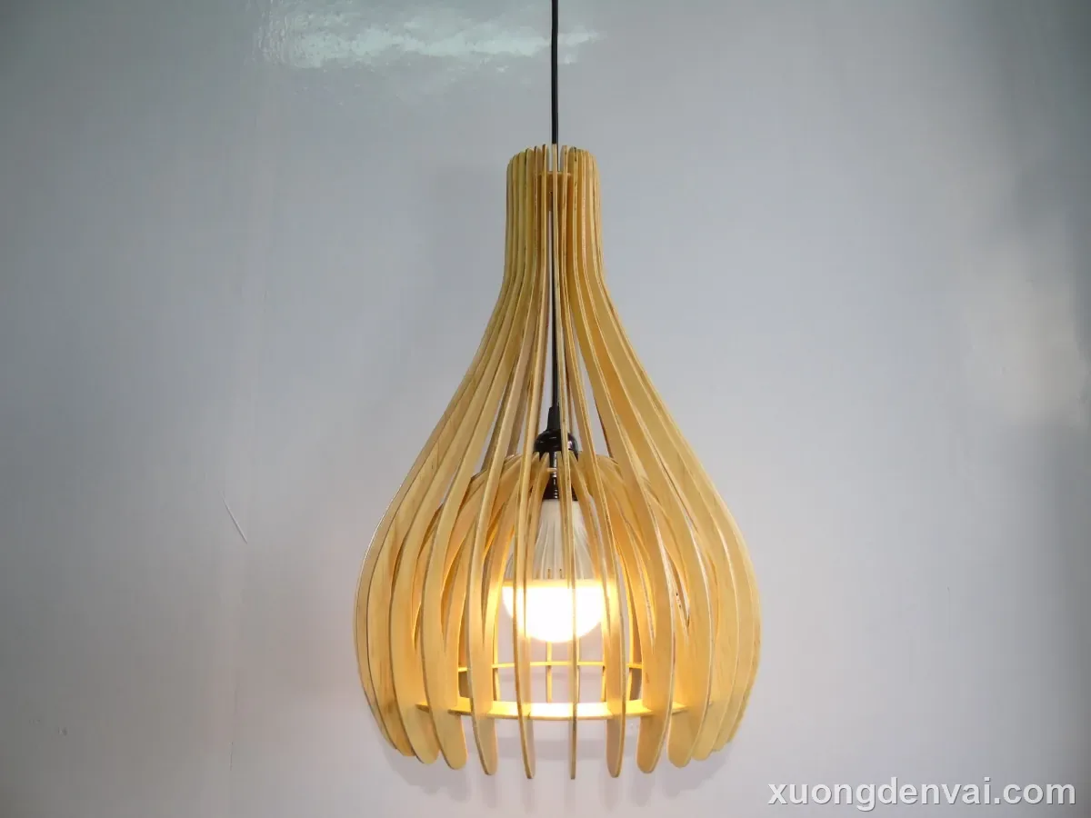 Đèn gỗ thả trần dáng giọt nước, các nan gỗ vàng nhạt uốn cong phình rộng phía đáy và thu nhỏ dần lên phần cổ đèn