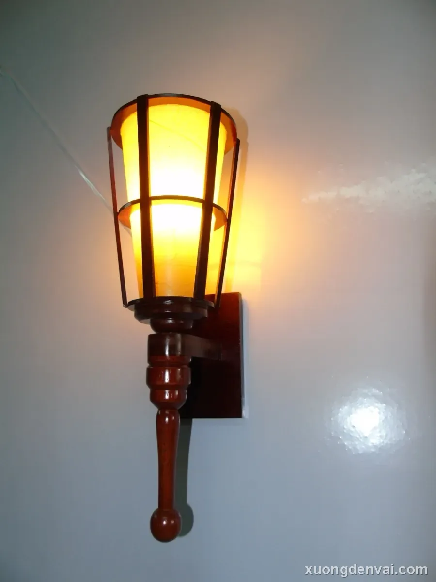 Đèn lồng gỗ cổ điển màu nâu trầm, khung chạm với mặt kính mờ hai tầng, treo trên tay đỡ gỗ tiện gắn tường