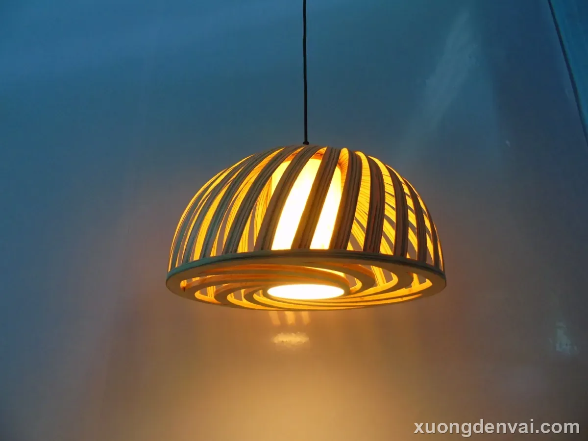 Đèn lồng gỗ thả trần dáng mái vòm bán cầu, nan gỗ cong đan hướng tâm, bóng đèn sợi đốt lộ ra giữa lòng đèn