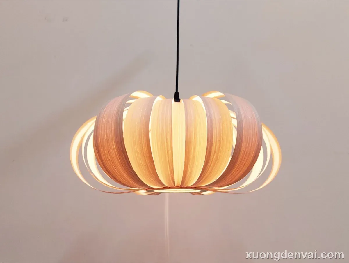 Đèn thả trần gỗ dáng quả thông thuôn dài như giọt nước, các vảy gỗ nhọn xếp lớp, ánh sáng vàng nổi bật trên nền tối