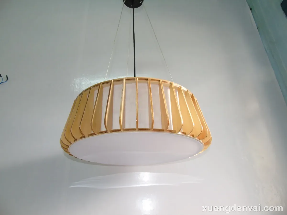 Đèn thả trần gỗ dáng trống tròn dẹt, nan gỗ dựng đều quanh viền, đáy kính mờ trắng tỏa sáng, treo bằng dây cáp