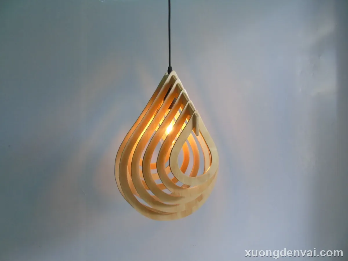 Đèn thả trần gỗ với 5 lớp nan gỗ xoắn lồng vào nhau tạo dáng giọt nước, ánh sáng vàng ấm lệch tầng giữa các lớp nan